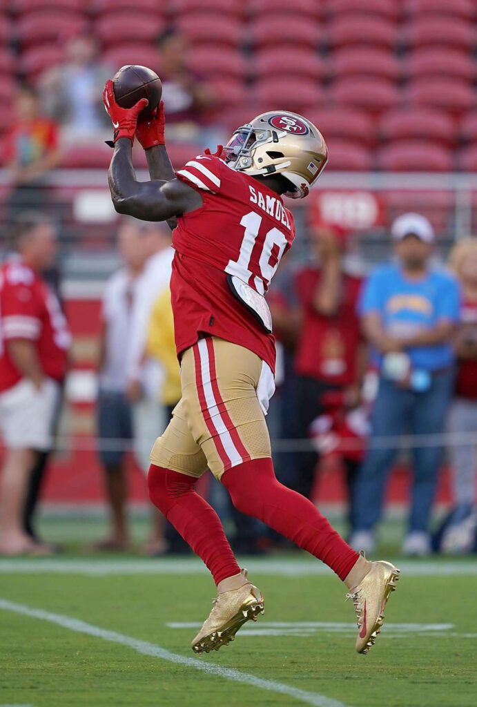 Deebo Samuel 49ers making a high catch leaping in red gold uniform on football field action shot Wallpaper