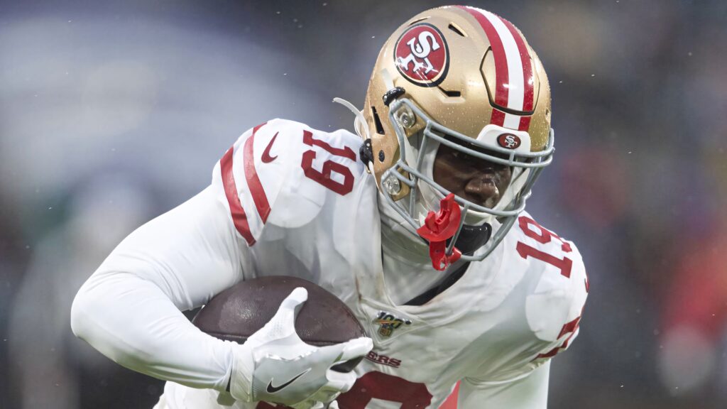 Deebo Samuel Sr running powerfully in red and gold 49ers uniform during dynamic football game Wallpaper