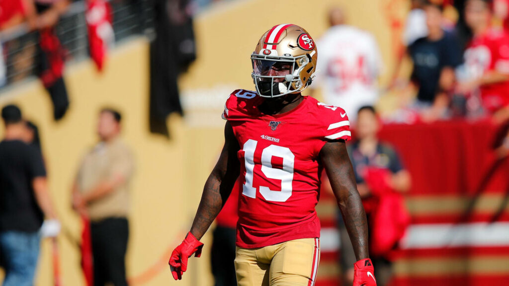 Deebo Samuel Sr in red and yellow San Francisco 49ers uniform on sunlit stadium field game day Wallpaper
