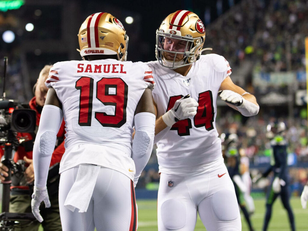 Deebo Samuel and Kyle Juszczyk celebrate in San Francisco 49ers uniforms under stadium lights Wallpaper