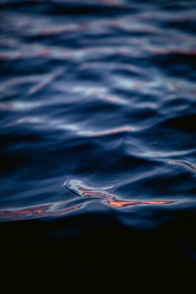 Dark blue water surface with gentle waves and ripples creating a calm moody wallpaper background
