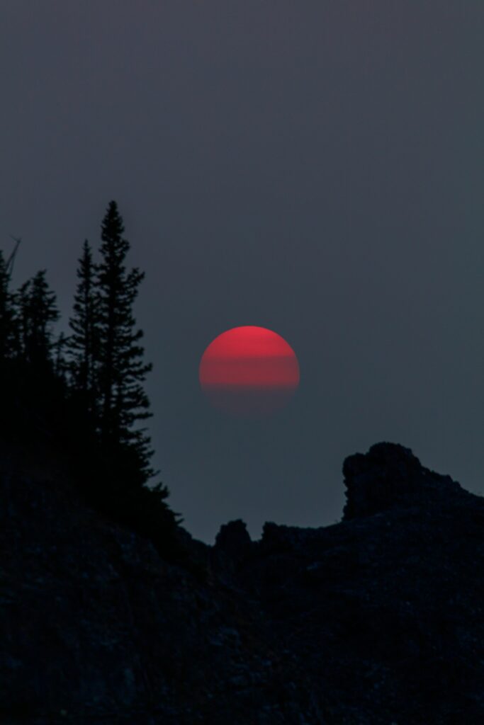 Striking red sunset over silhouetted trees and rocks against dusky evening sky wallpaper background
