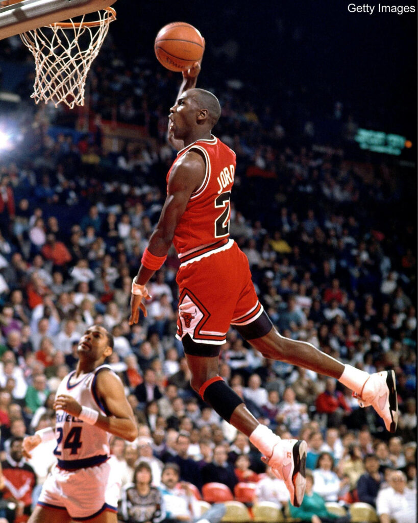 Soaring through air: Michael Jordan defies gravity in an awe-inspiring mid-flight moment. Wallpaper