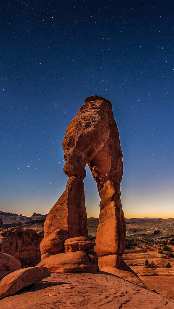 Side view of Delicate Arch glowing golden under starry night sky desert landscape wallpaper