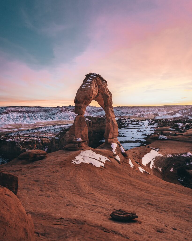 Delicate Arch at sunset with sandstone tones snow patches and pastel evening sky wallpaper background
