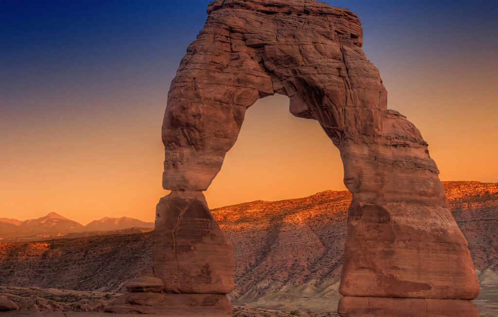 Delicate Arch at sunset with vibrant ombre sky over rugged desert landscape wallpaper background