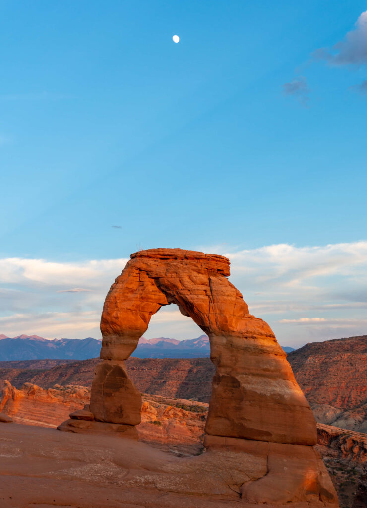 Delicate Arch at dawn glowing golden against clear blue sky over red desert terrain wallpaper