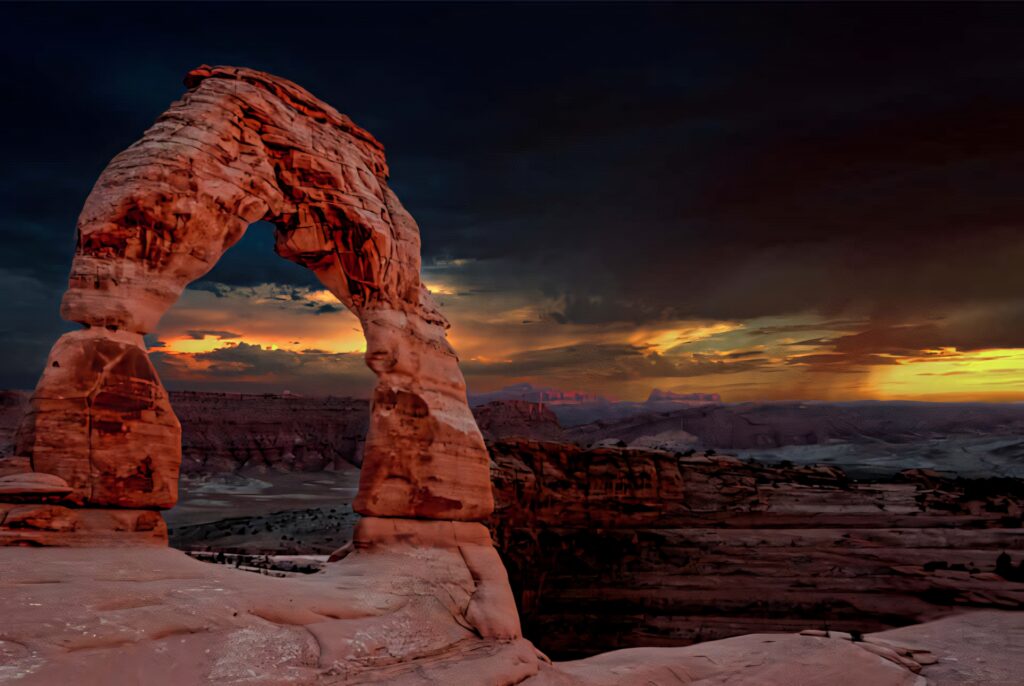 Delicate Arch glowing warm at sunset under dark stormy clouds dramatic sandstone landscape Wallpaper