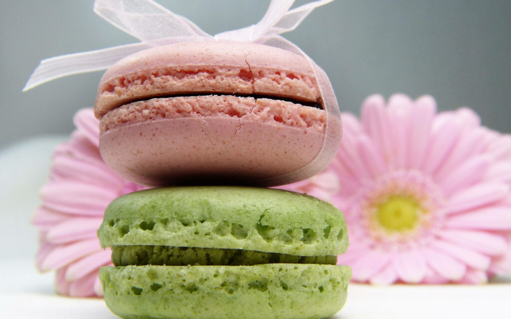 Dainty Delights: A Vibrant Stack of Macarons amidst Pink Daisy Bliss Wallpaper