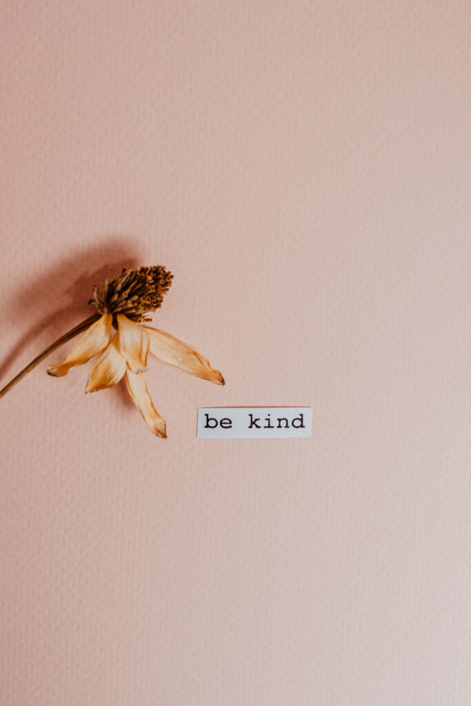 Delicate dried flower with be kind sticker on soft peach background inspiring wallpaper