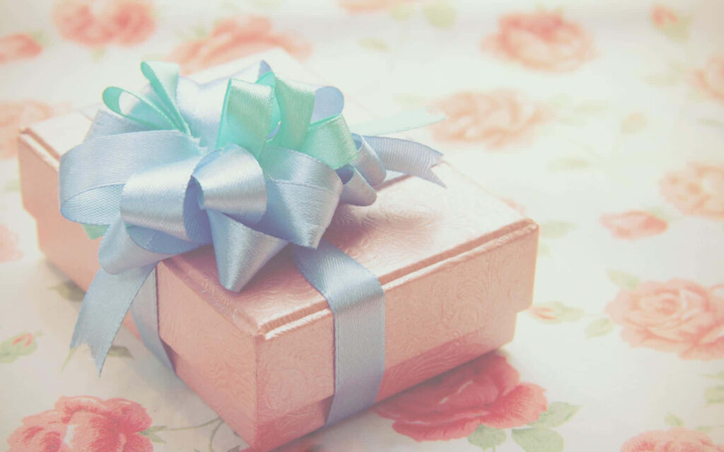 Delicate pink gift box with blue ribbon on floral surface perfect for celebration wallpaper background