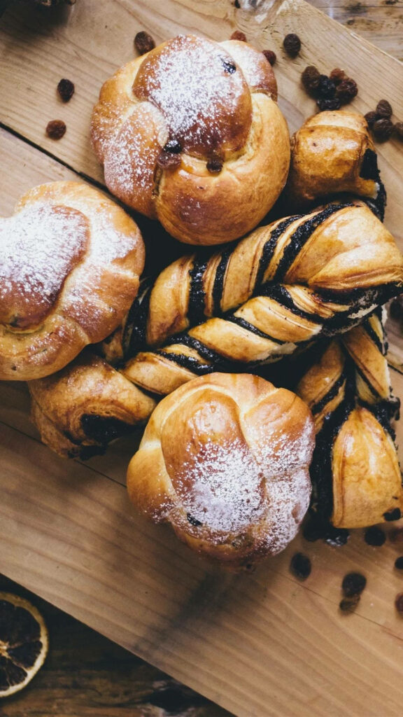 Assorted breads with golden sweet rolls chocolate swirl loaves and raisins on rustic wood surface Wallpaper