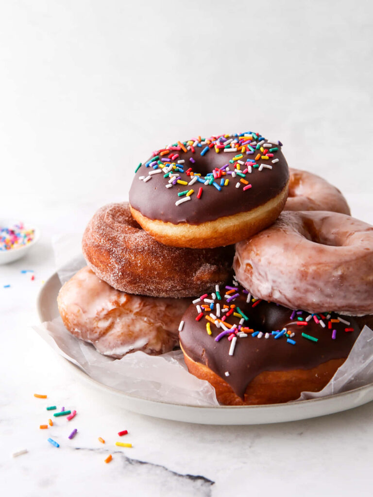 Stack of assorted donuts with chocolate glaze sprinkles sugar coating on bright soft background Wallpaper