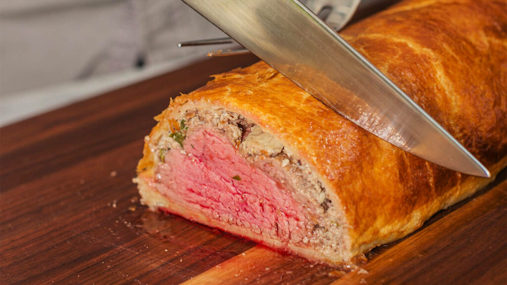 Sliced Beef Wellington showing tender pink center and golden flaky pastry on wallpaper background