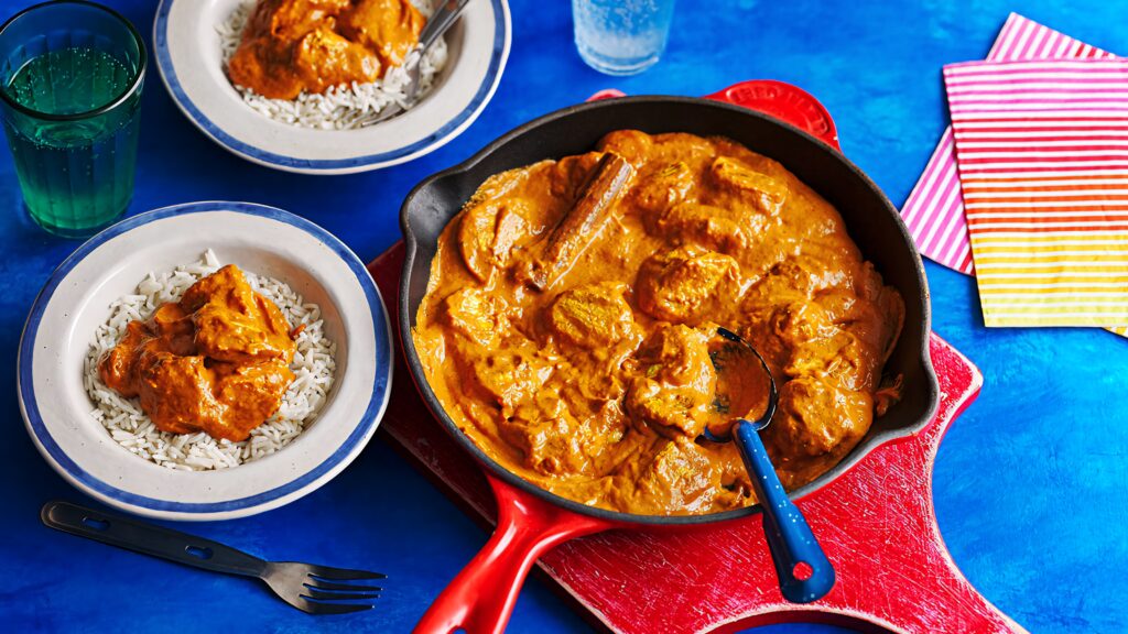 Butter chicken in creamy orange sauce with steamed rice in skillet on vibrant blue background wallpaper