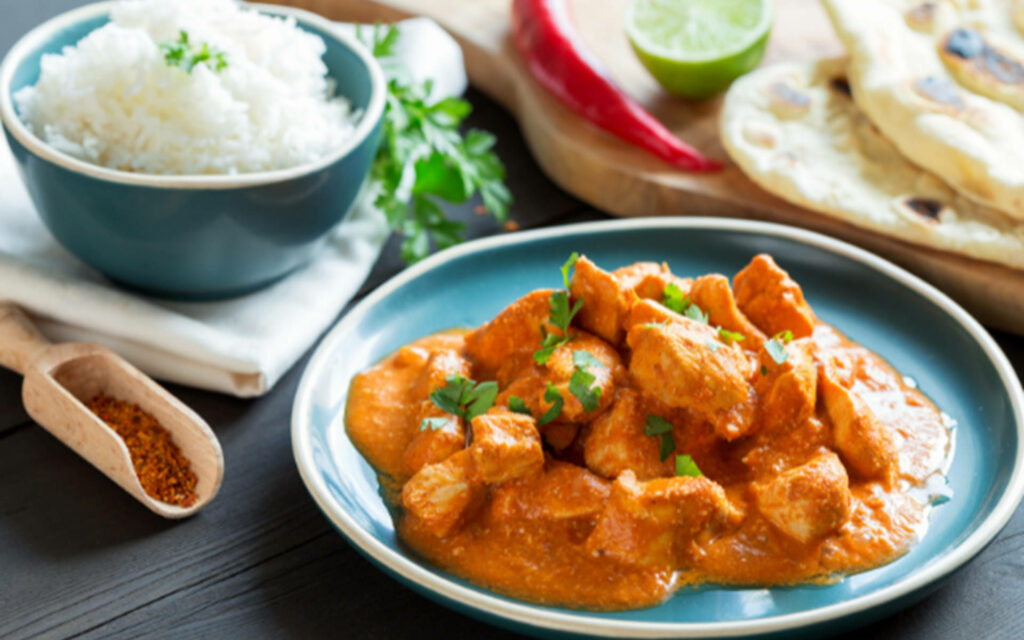 Butter chicken on blue plate with rich orange curry rice naan fresh herbs vibrant wallpaper