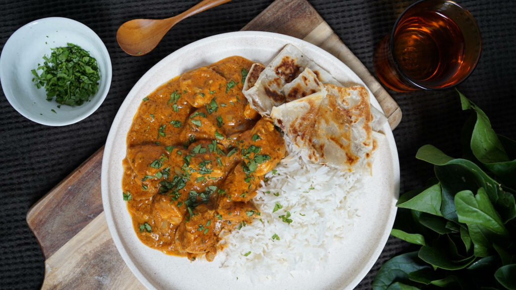 Butter chicken in creamy orange sauce with white rice and flatbread on rustic wooden table Wallpaper