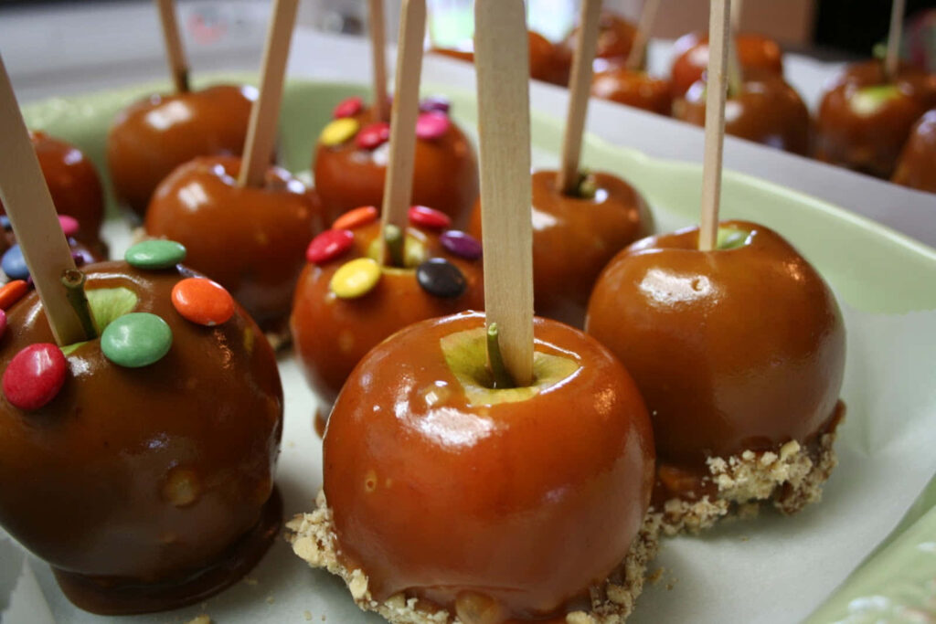 Glossy caramel apples with colorful candies and nuts on rustic wooden table background Wallpaper