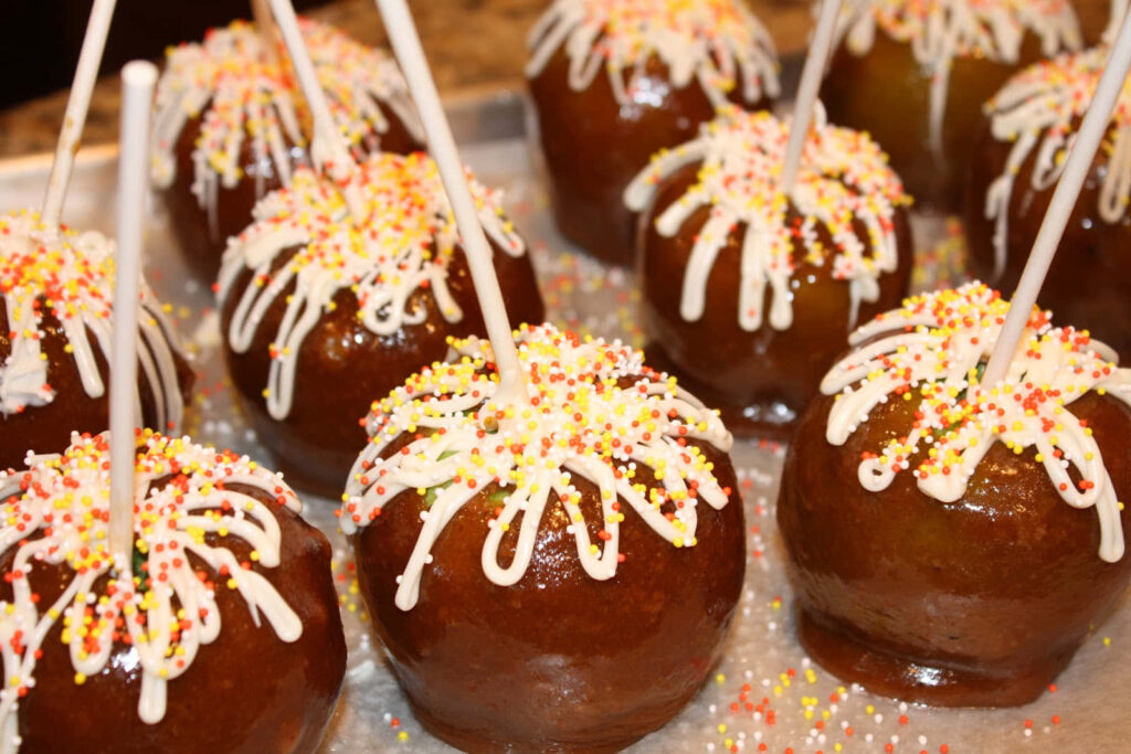 Glossy caramel apples drizzled with white chocolate and sprinkles on rustic wooden table wallpaper