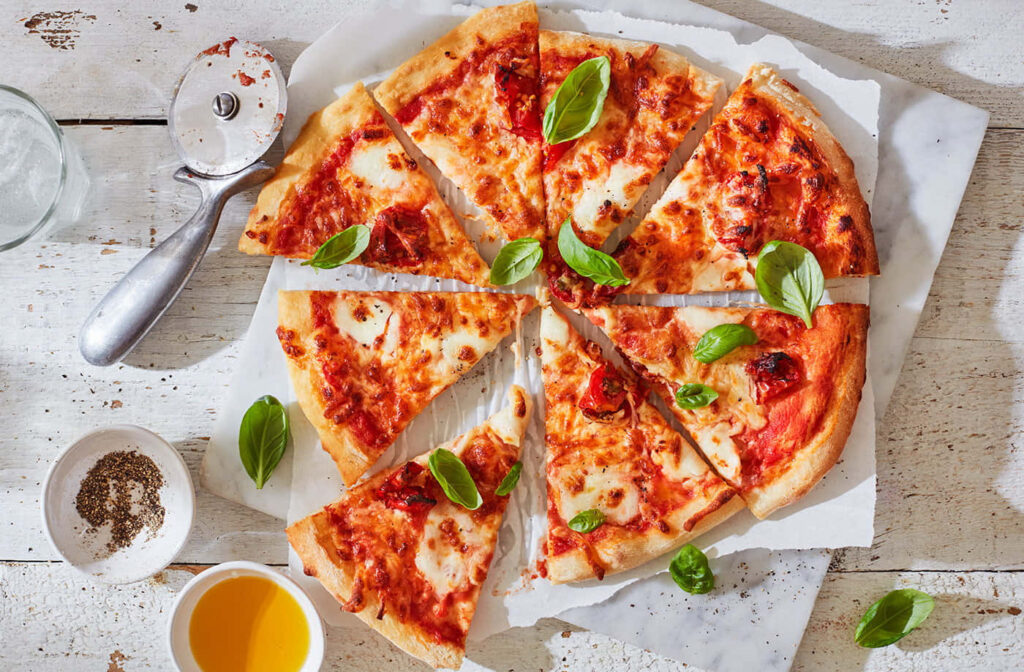 Cheese pizza with fresh basil sliced on rustic white table with olive oil black pepper and cutter Wallpaper