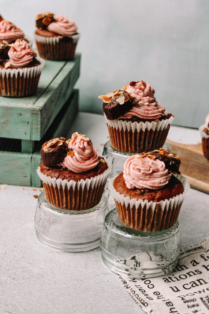 Choco almond cupcakes with pink frosting and almond slices on rustic pastel bakery wallpaper background