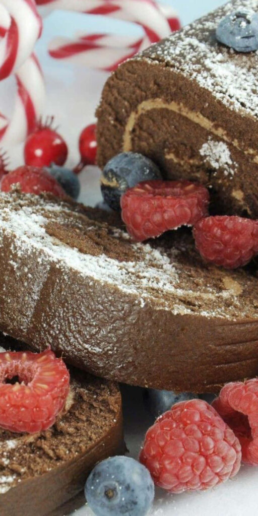 Sliced chocolate cake roll with powdered sugar fresh raspberries and blueberries festive dessert background Wallpaper