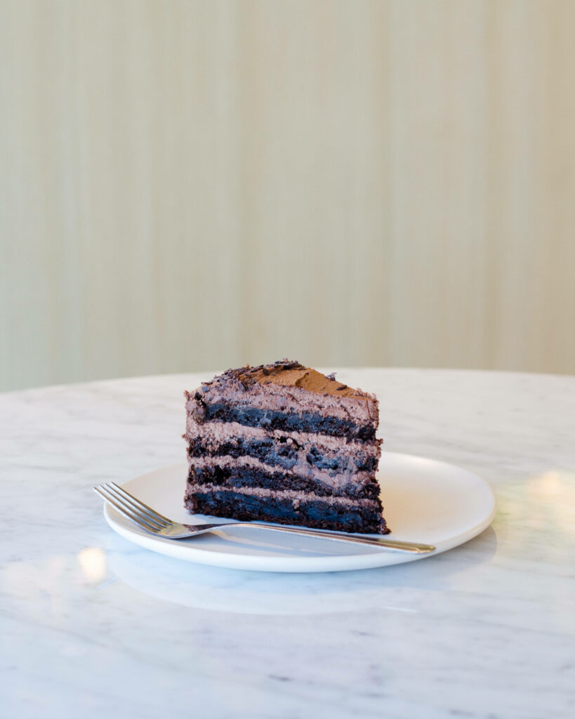 Rich chocolate cake slice with creamy layers on white plate marble table dessert background Wallpaper
