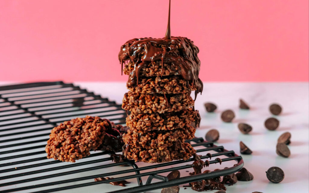 Stack of homemade chocolate cookies drizzled with melted chocolate on pink background with chips Wallpaper