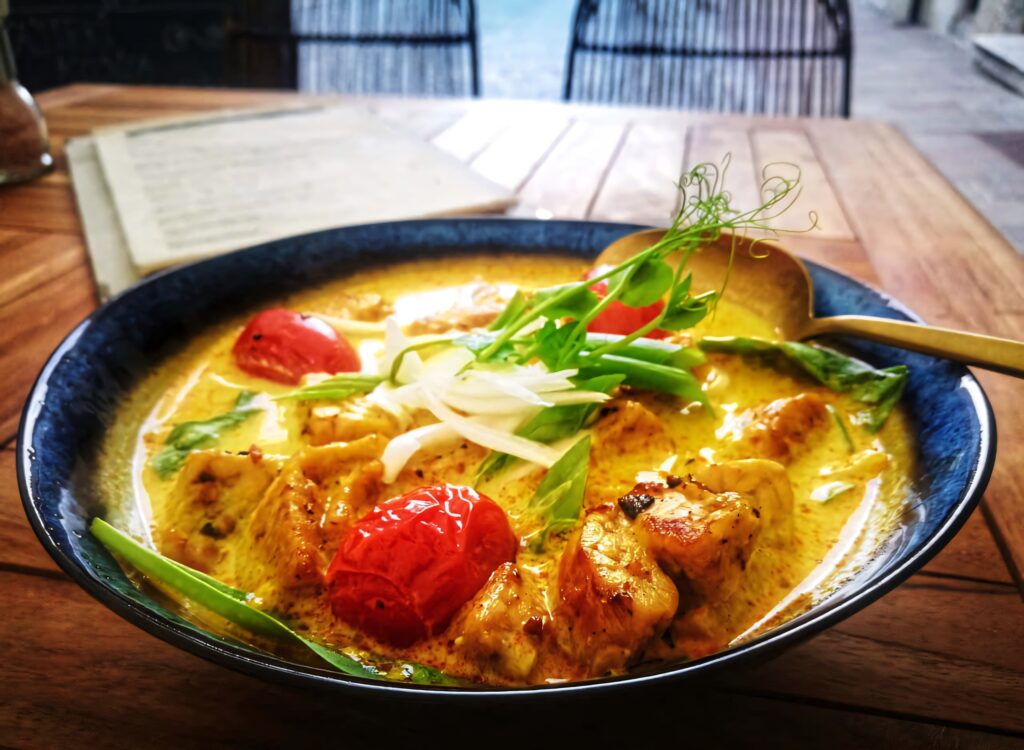 Bowl of creamy curry laksa with chicken fresh greens roasted tomatoes on rustic wood background Wallpaper