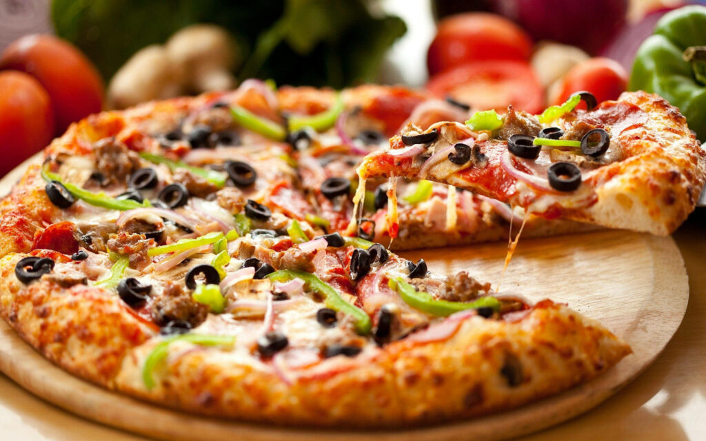 Hand-tossed Domino's pizza with green peppers black olives onions melted cheese on wood background Wallpaper