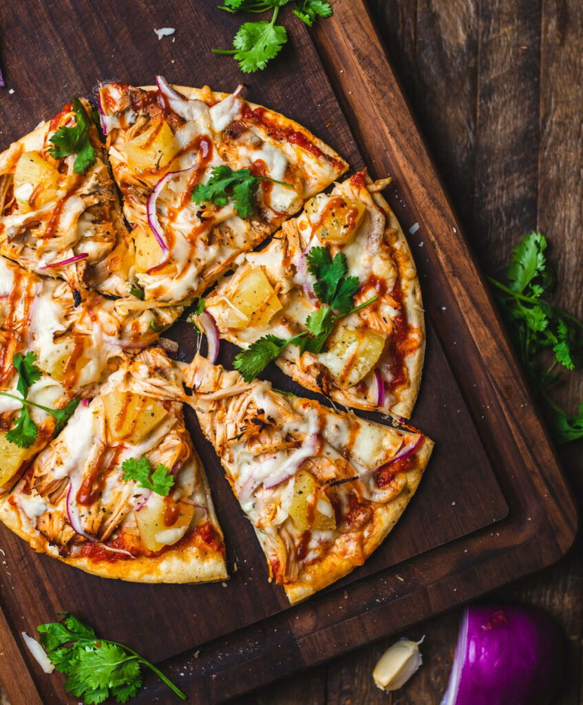 Dominos pizza with basil pineapple onions melted cheese on rustic wooden board wallpaper background
