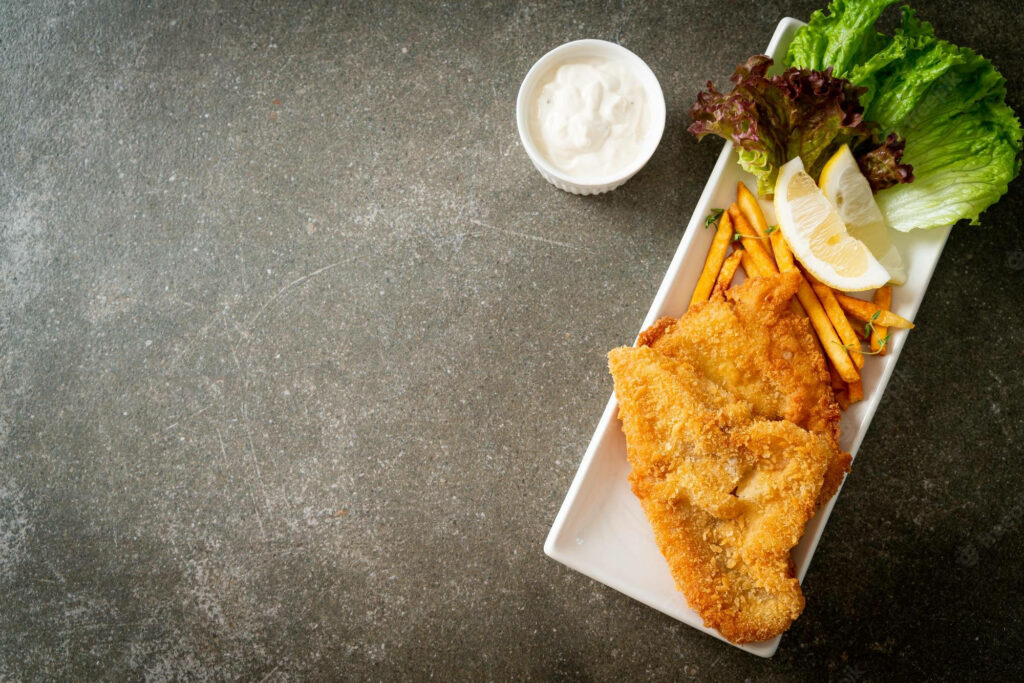 Delicious Fish and Chips Close-Up with Fresh Garnishes & Rustic Background Wallpaper
