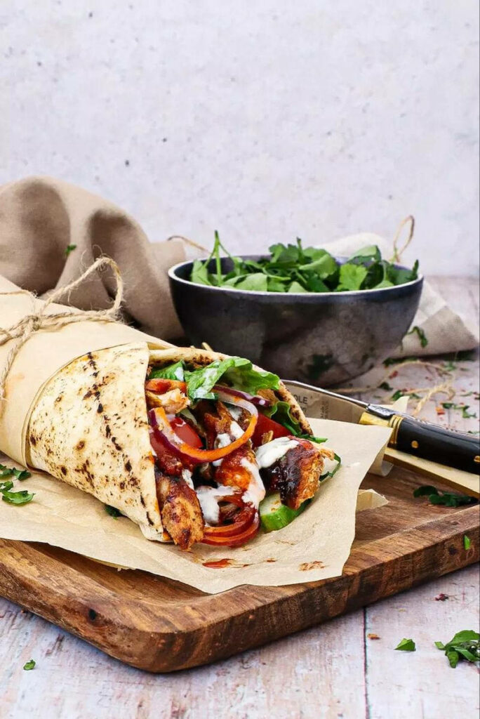 Juicy grilled chicken burrito wrapped in flatbread with fresh vegetables on rustic wood Wallpaper