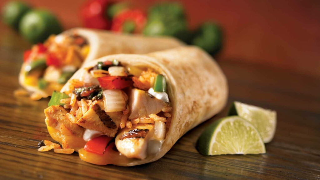 Closeup vibrant rice and meat burrito with grilled chicken peppers onions lime wedges wallpaper background