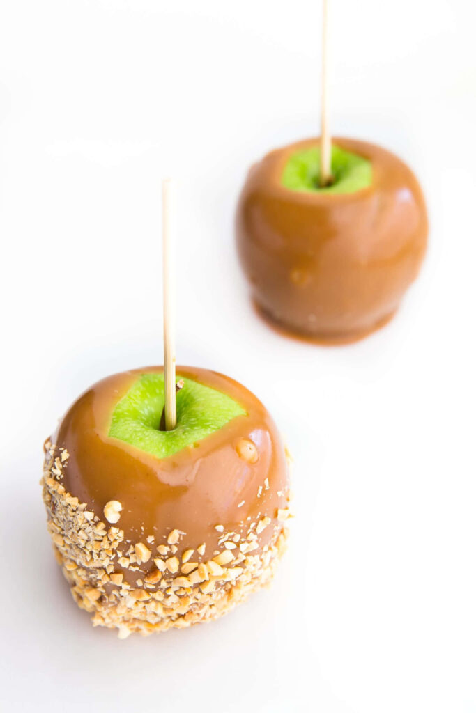 Two homemade caramel apples one with nuts one smooth on white background autumn treat wallpaper