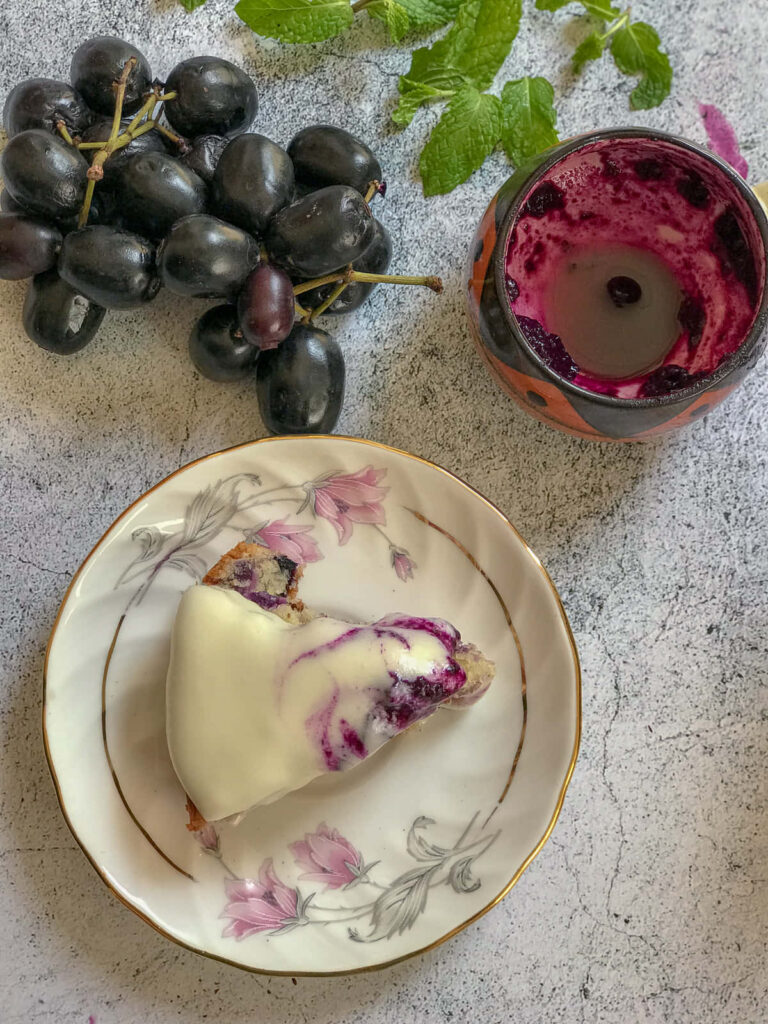 Slice of Java plum cake with white icing on floral saucer fresh Java plums vibrant purple residue Wallpaper