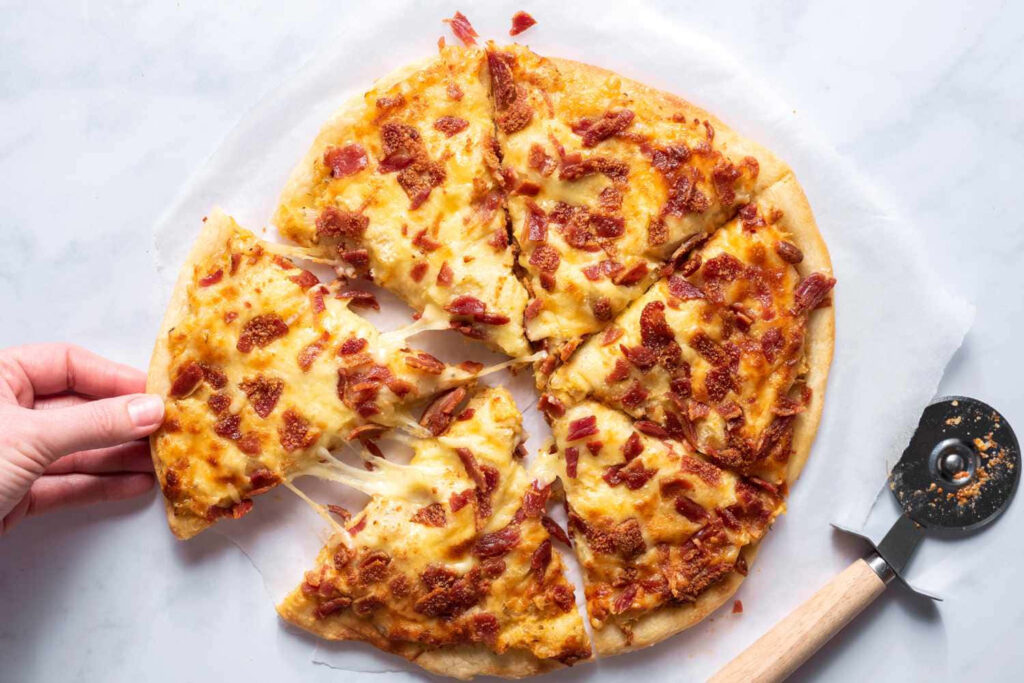 Freshly baked gooey cheese and diced ham pizza slice being pulled from plate on wallpaper background