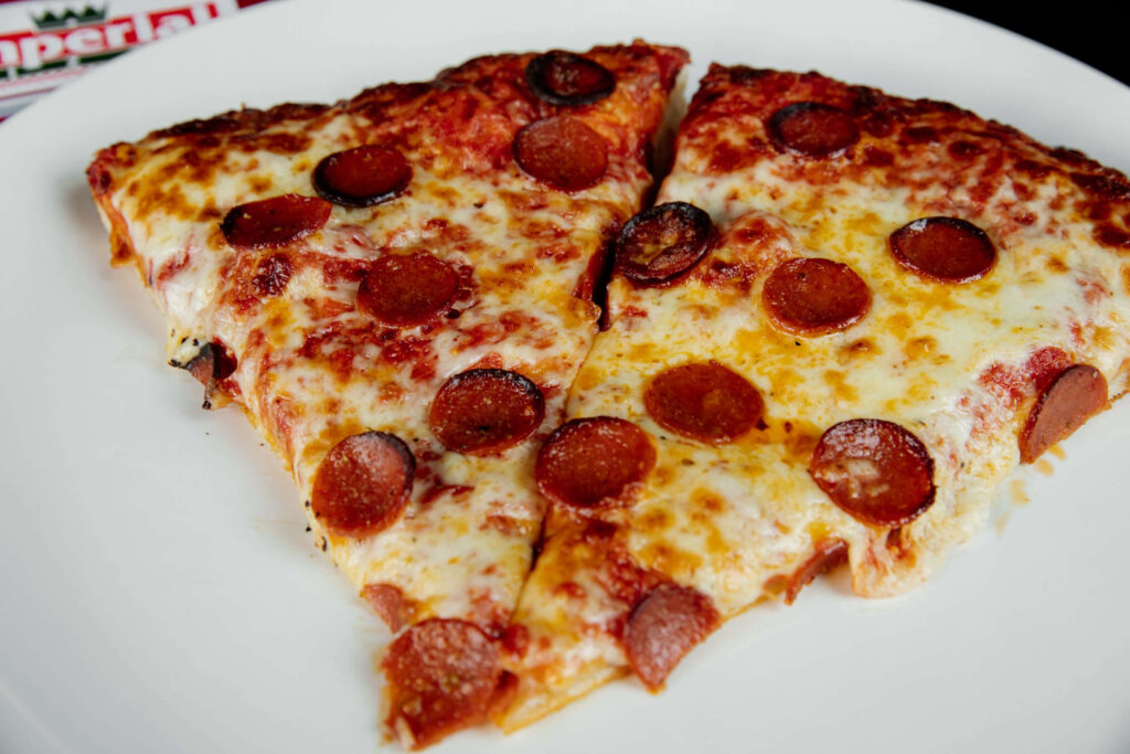 Two pepperoni pizza slices with melted cheese on a white plate against wallpaper background