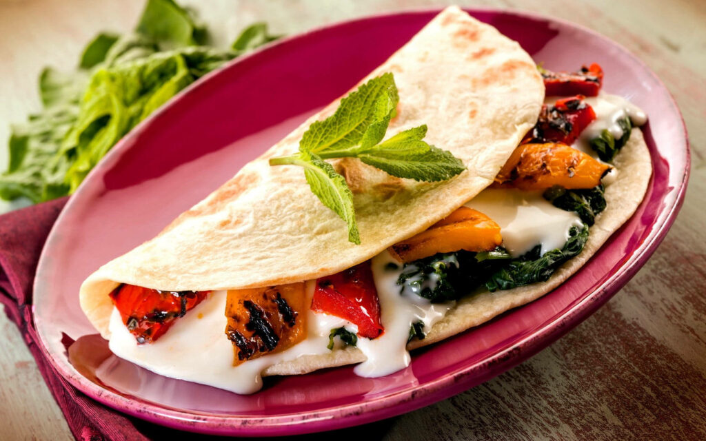 Vibrant roti burrito with grilled vegetables and melted cheese on scarlet plate with herbs wallpaper background