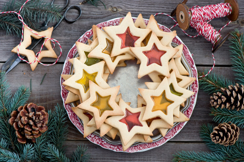 Festive Delights: Vibrant Star-shaped Cookies Adorn a Scarlet Plate Amidst a Whimsical Foliage Backdrop Wallpaper