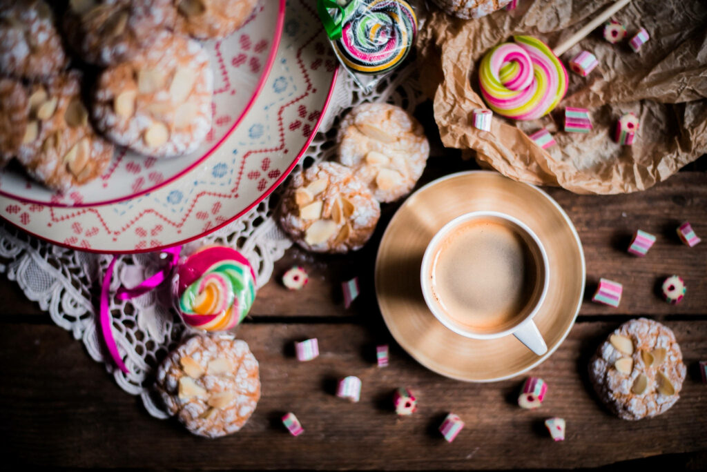 A Scrumptious Still Life: Sweet Amaretti, Vibrant Candies, and a Steamy Cup of Coffee Wallpaper