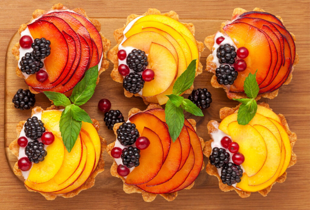 Delightful Spring Sweets: A Kaleidoscope of Vibrant Desserts, Crafted Elegantly on a Rustic Wooden Table Adorned with Fresh Blooms and Luxurious Foliage Wallpaper