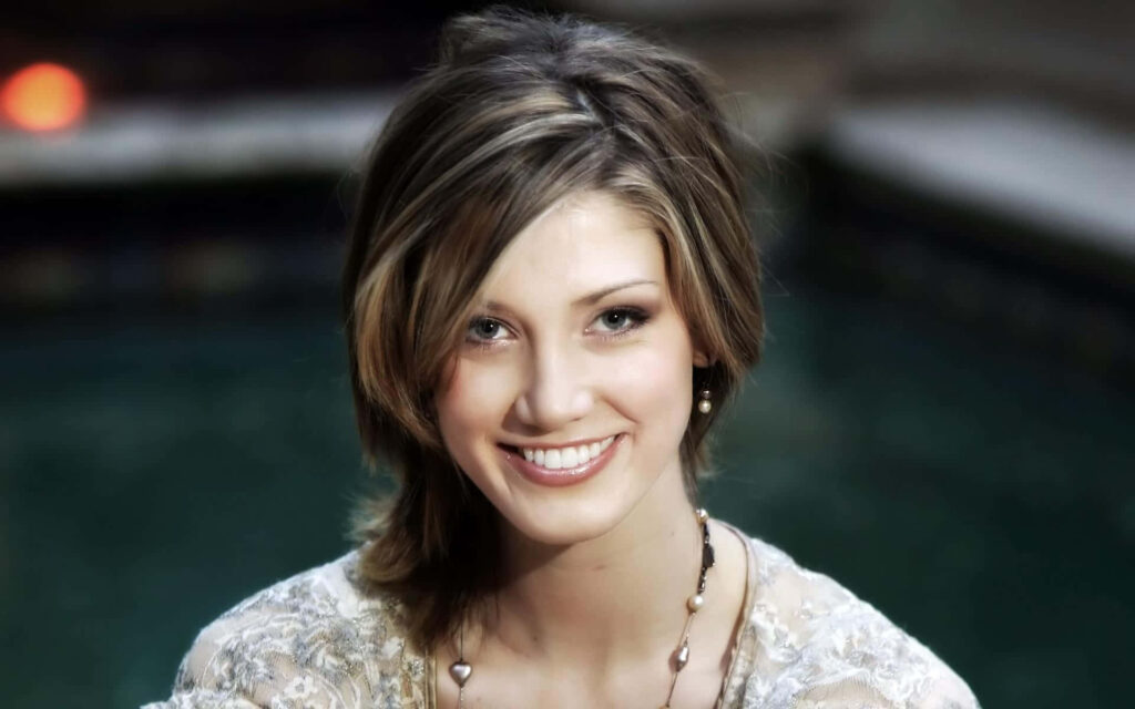 Delta Goodrem close-up portrait with radiant smile soft natural lighting green brown background Wallpaper
