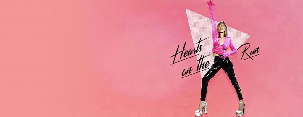Delta Goodrem in shiny pink top and black pants against soft pink geometric Hearts on the Run background Wallpaper