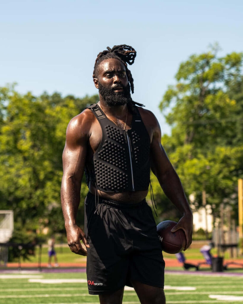 Demario Davis focused on football field training wearing performance vest holding football outdoors Wallpaper