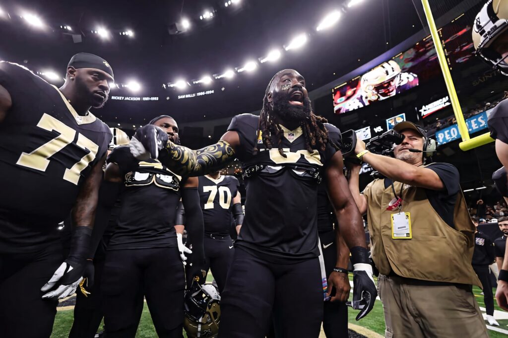 Demario Davis leads New Orleans Saints team huddle in black and gold uniforms under stadium lights Wallpaper