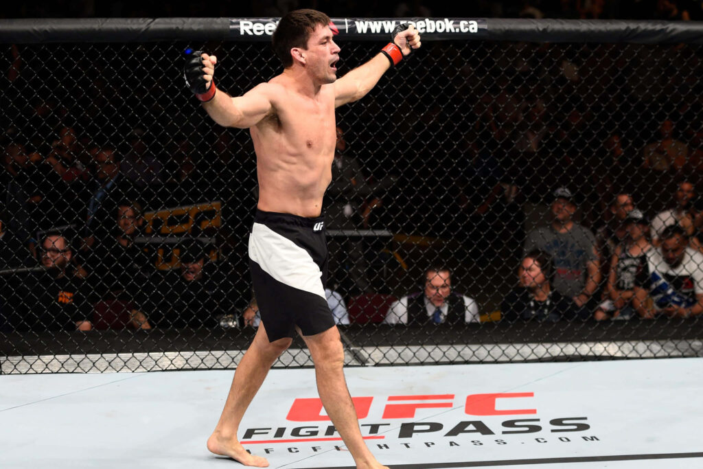 Demian Maia celebrating victory in UFC Octagon fight with intense arena lighting background Wallpaper