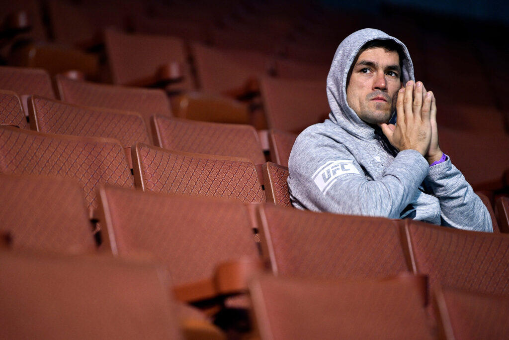 Demian Maia sitting alone in empty arena wearing grey UFC hoodie calm reflective moment wallpaper