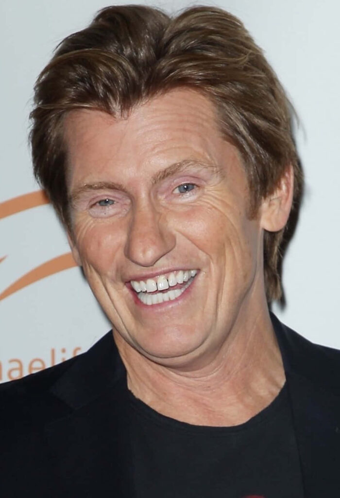Comedian Denis Leary smiling naturally in black attire on a neutral background wallpaper background