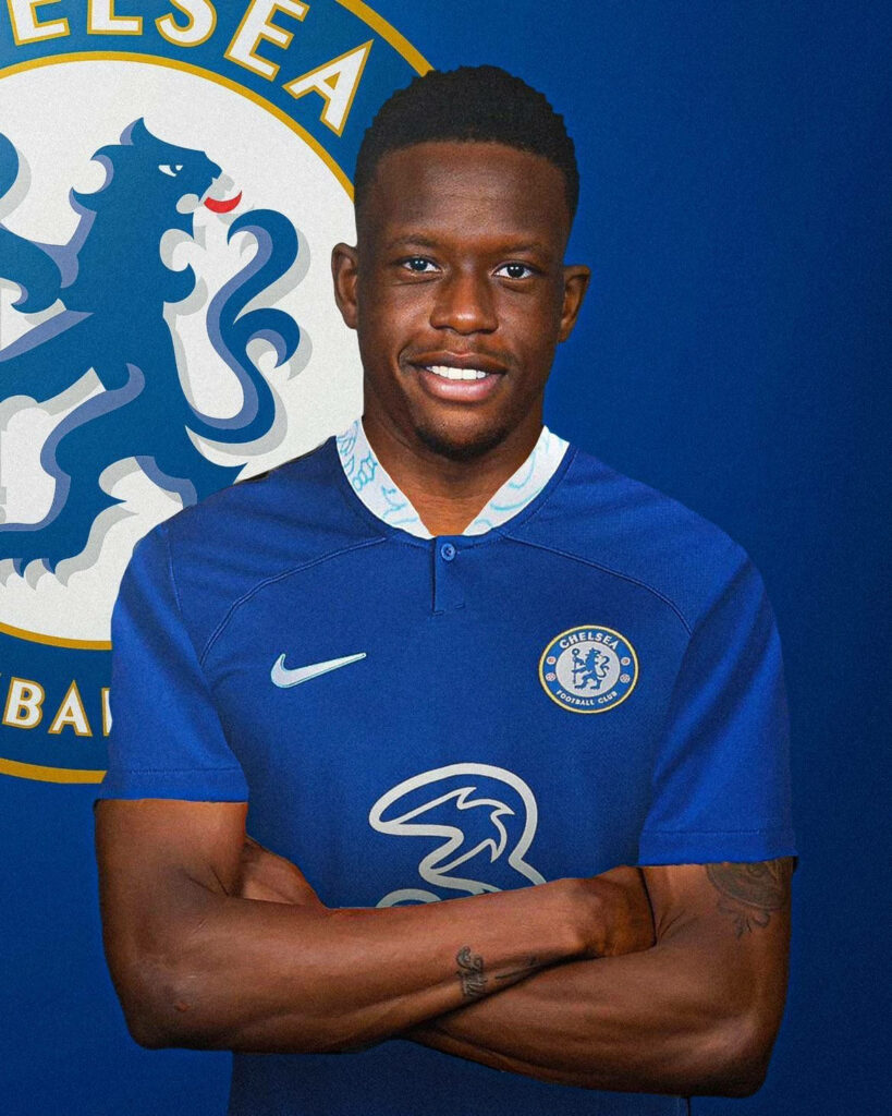 Denis Zakaria in Chelsea blue kit standing with arms crossed in front of Chelsea FC emblem wallpaper